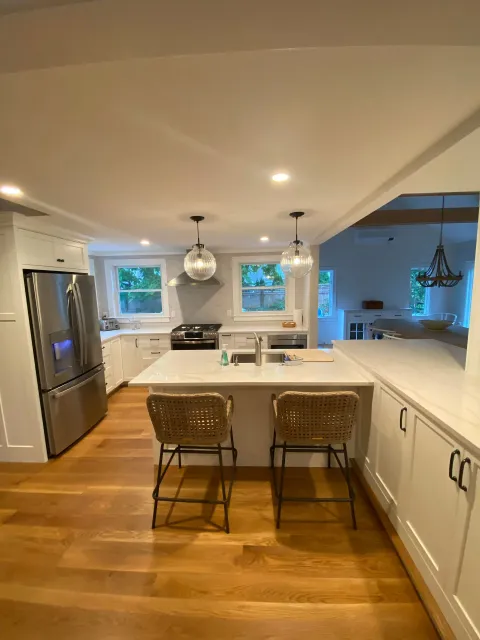 A kitchen with white cabinets, stainless steel appliances, wooden floors, and a large island