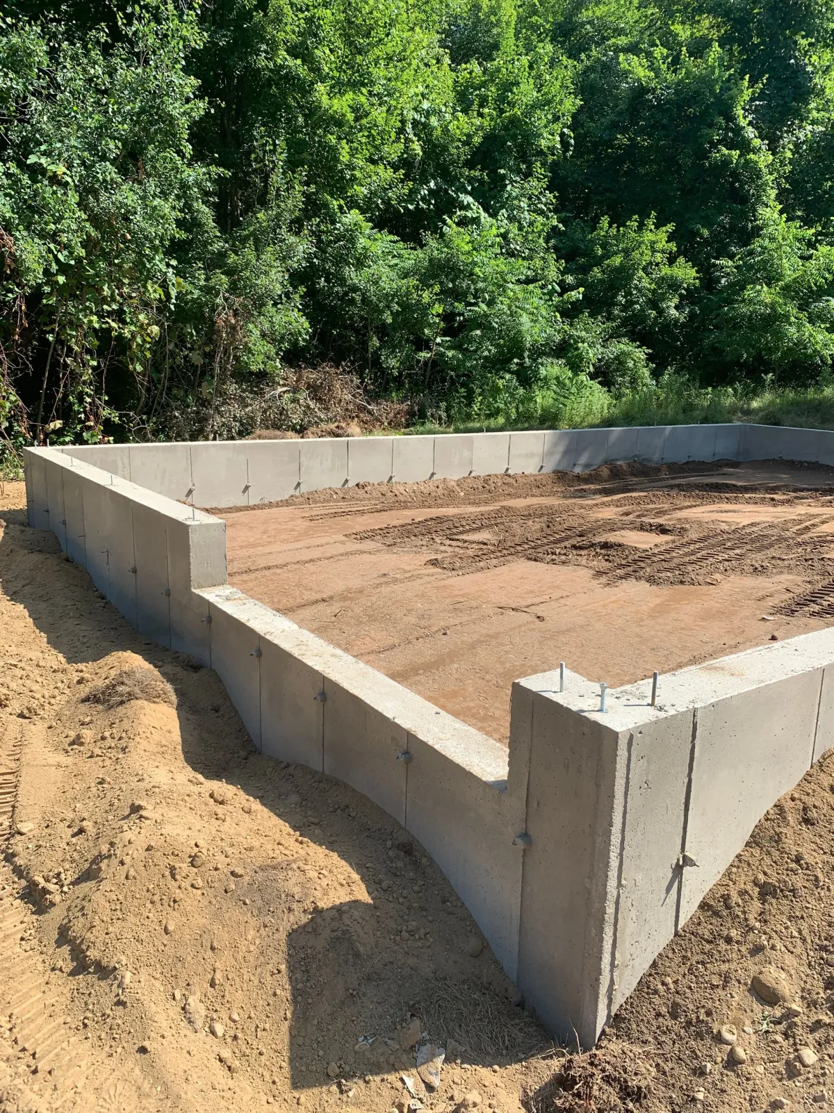 A concrete foundation is being built in a dirt field with trees in the background.