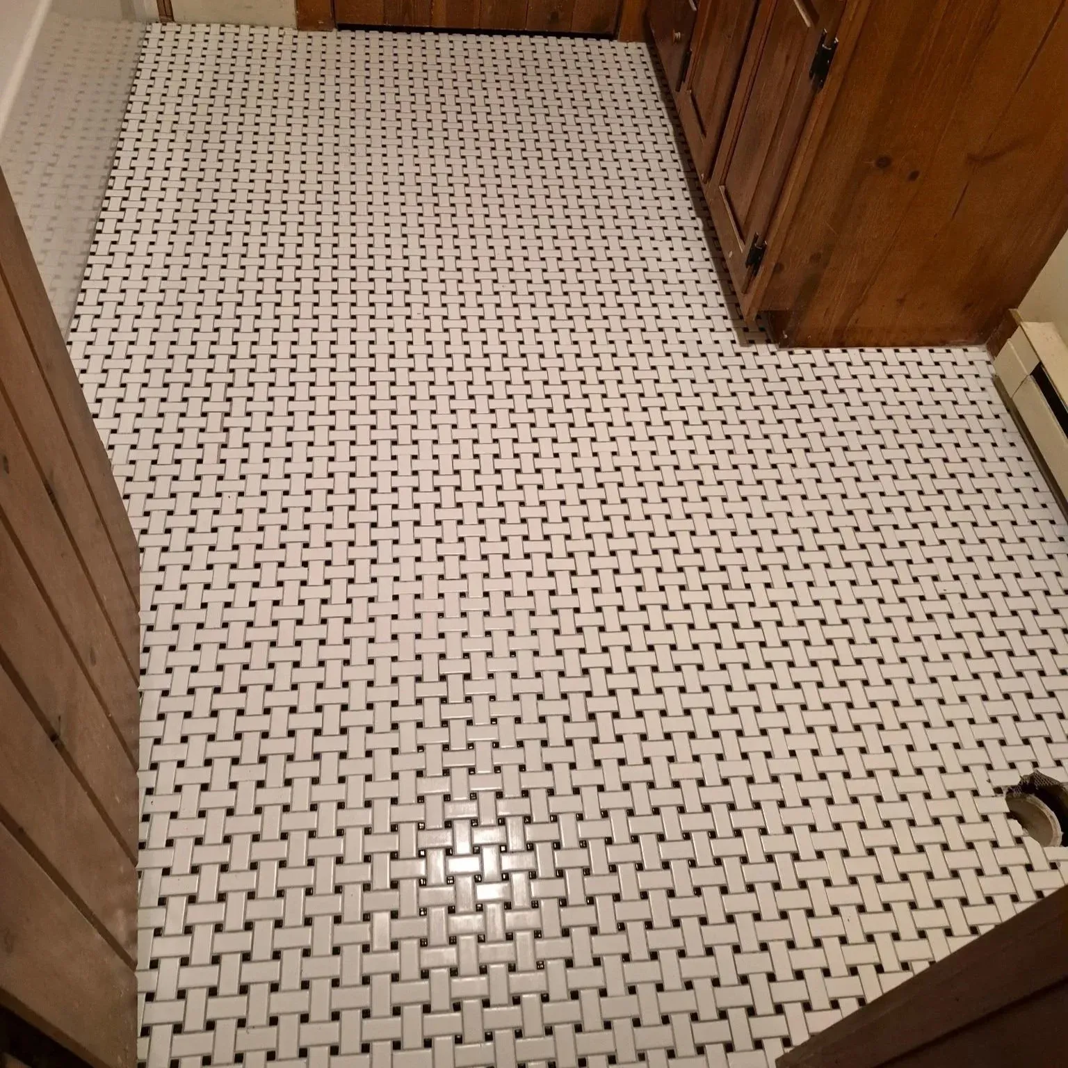 A kitchen floor with a white woven tile pattern, wooden kitchen cabinets, and a baseboard heater along the wall.
