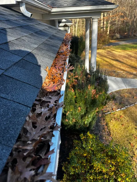 Gutter packed with debris along a roof edge before service