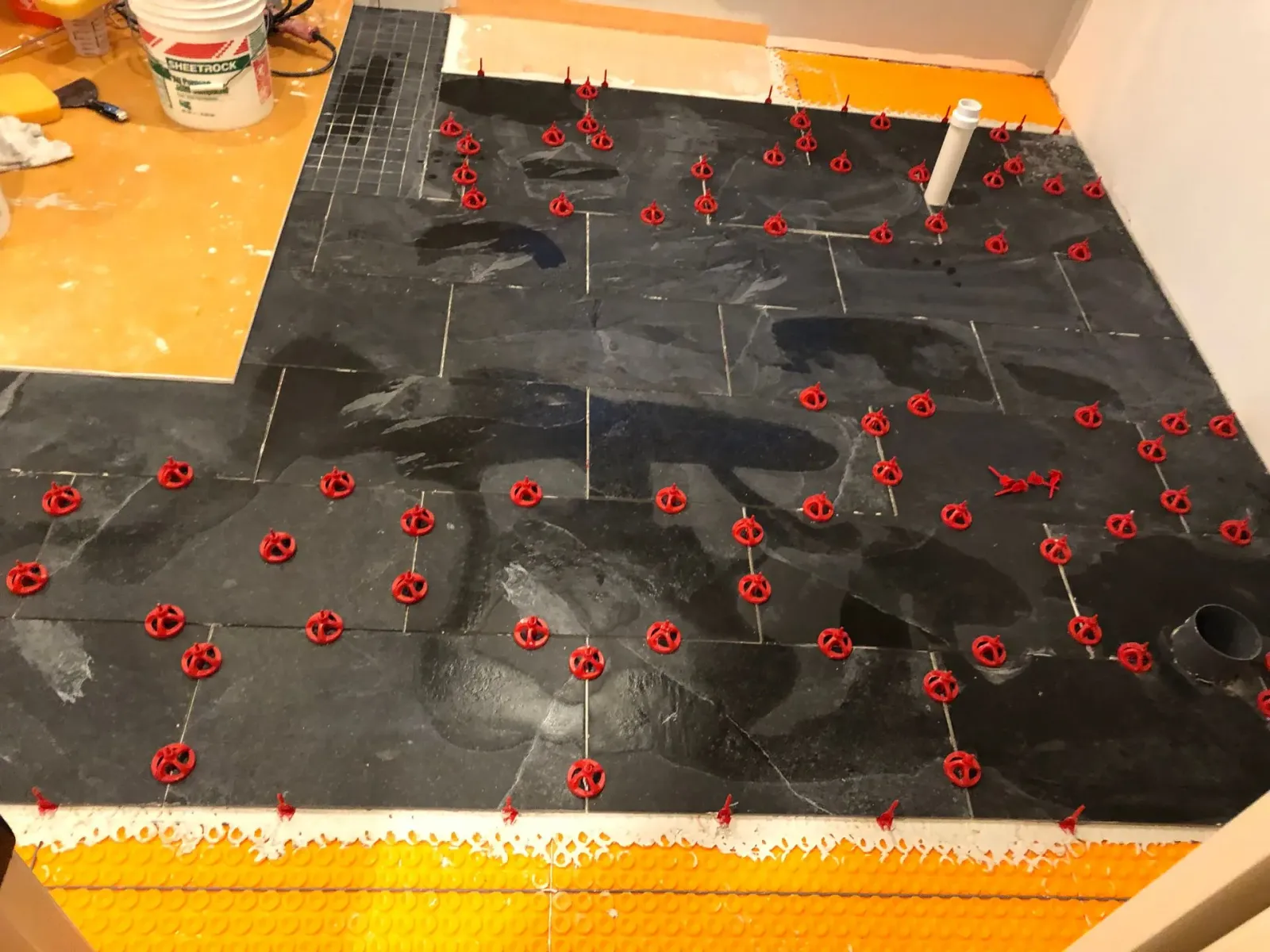 Black tiled floor under construction with many red tile spacers and white leveling clips around the edges.