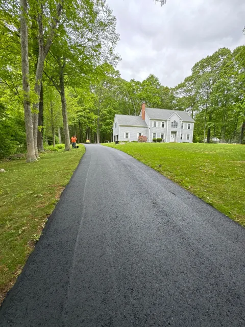 Gravel driveway lined with green trees leading to a white house on a cloudy day