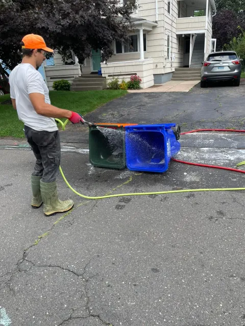A man is cleaning a trash can with a hose.