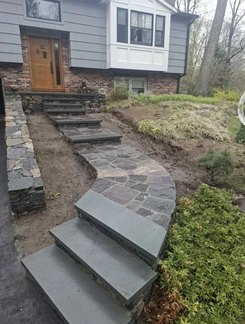 Finished bluestone front steps and walkway with a hand-laid natural stone wall, built by M&N Masonry
