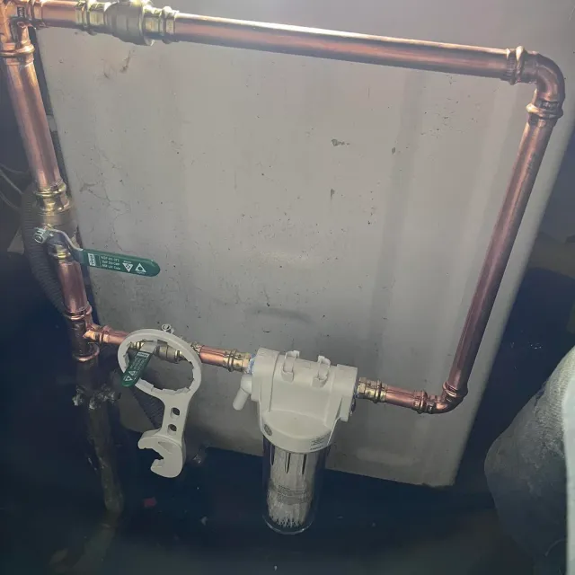 A whole-house water filter housing plumbed into a copper main with isolation valves either side.
