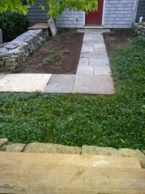 Front walkway of stone pavers leading to a red door, with grass, a small garden bed, and a stone wall.