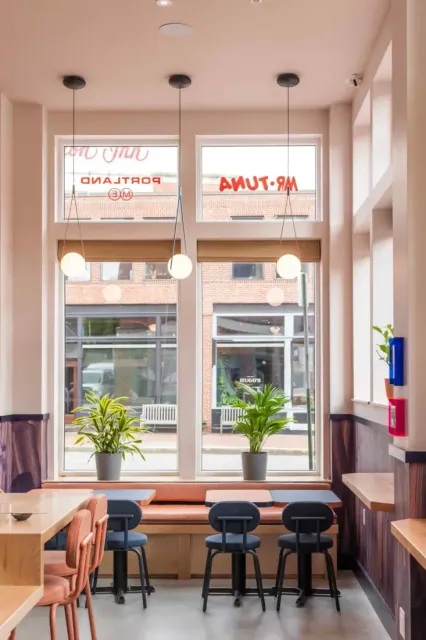 Detail view of Mr. Tuna’s interior designed by Woodhull Architects, featuring a curved wood counter, soft pink walls, and warm ambient lighting