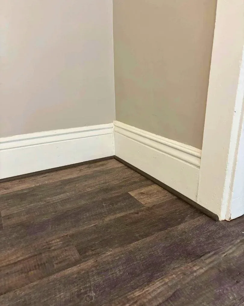 Close-up of dark luxury vinyl plank flooring installed along white baseboards and trim, showcasing clean edges, detailed finishing work, and a realistic wood-look texture by JK Flooring & Tile.