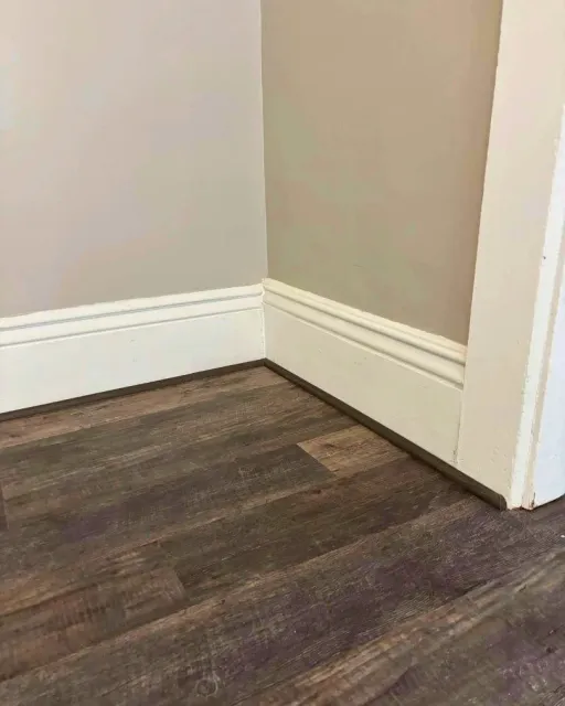 Close-up of dark luxury vinyl plank flooring installed along white baseboards and trim, showcasing clean edges, detailed finishing work, and a realistic wood-look texture by JK Flooring & Tile.
