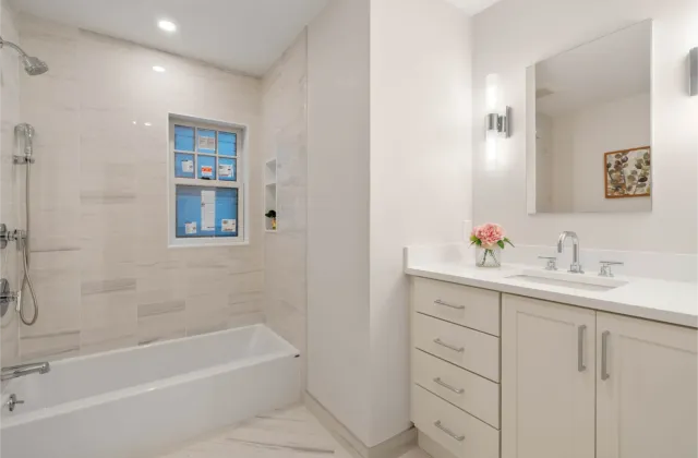 Modern bathroom with a bathtub, large mirror, white cabinets, and a vase with pink flowers on the counter.