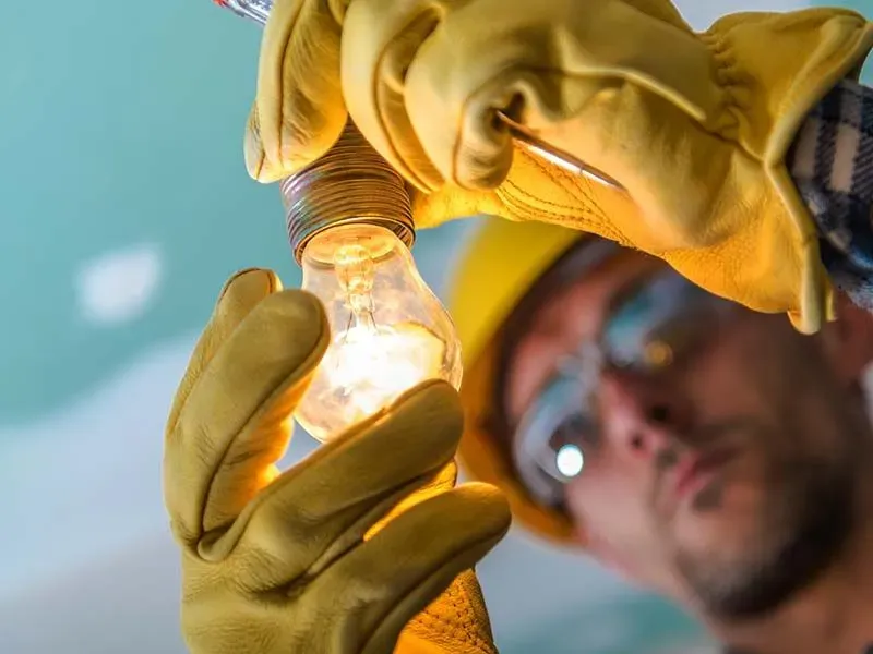 A man in a hard hat and gloves is fixing a light bulb.