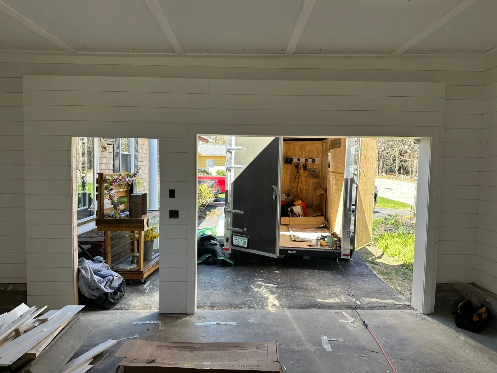 A garage with an open bay door, showing a trailer outside and household items inside.