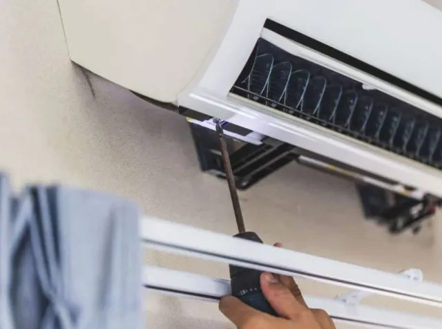 Person using a screwdriver to repair a wall-mounted air conditioner