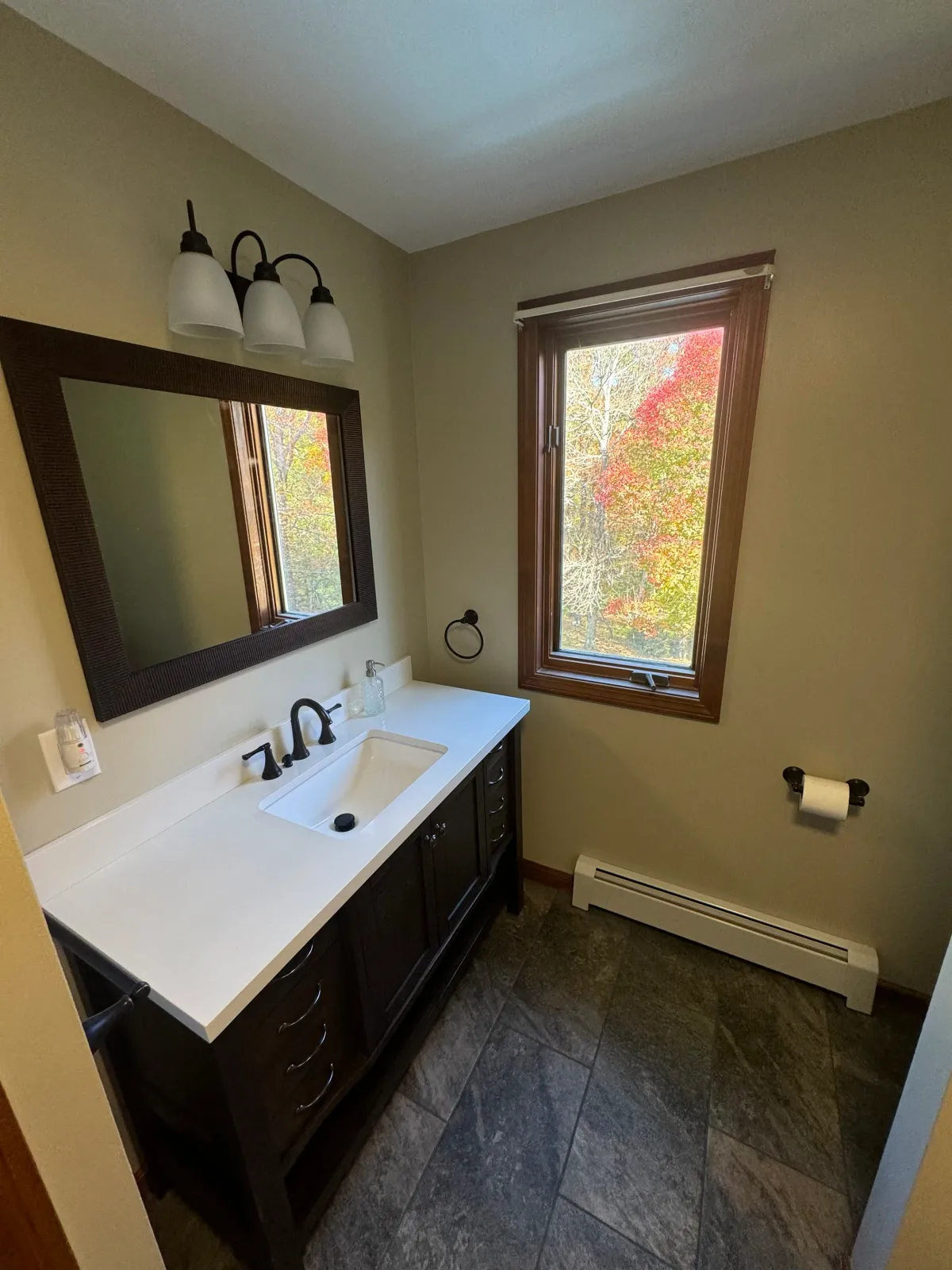 Small bathroom with a vanity, mirror, and window showing fall foliage outside.