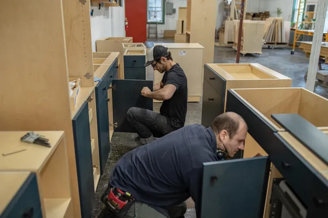 Two cabinetmakers building blue cabinetry in a workshop