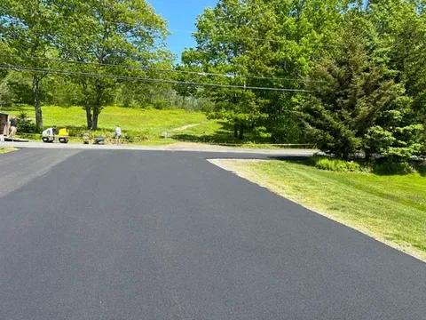 Newly paved asphalt driveway with green trees and grass