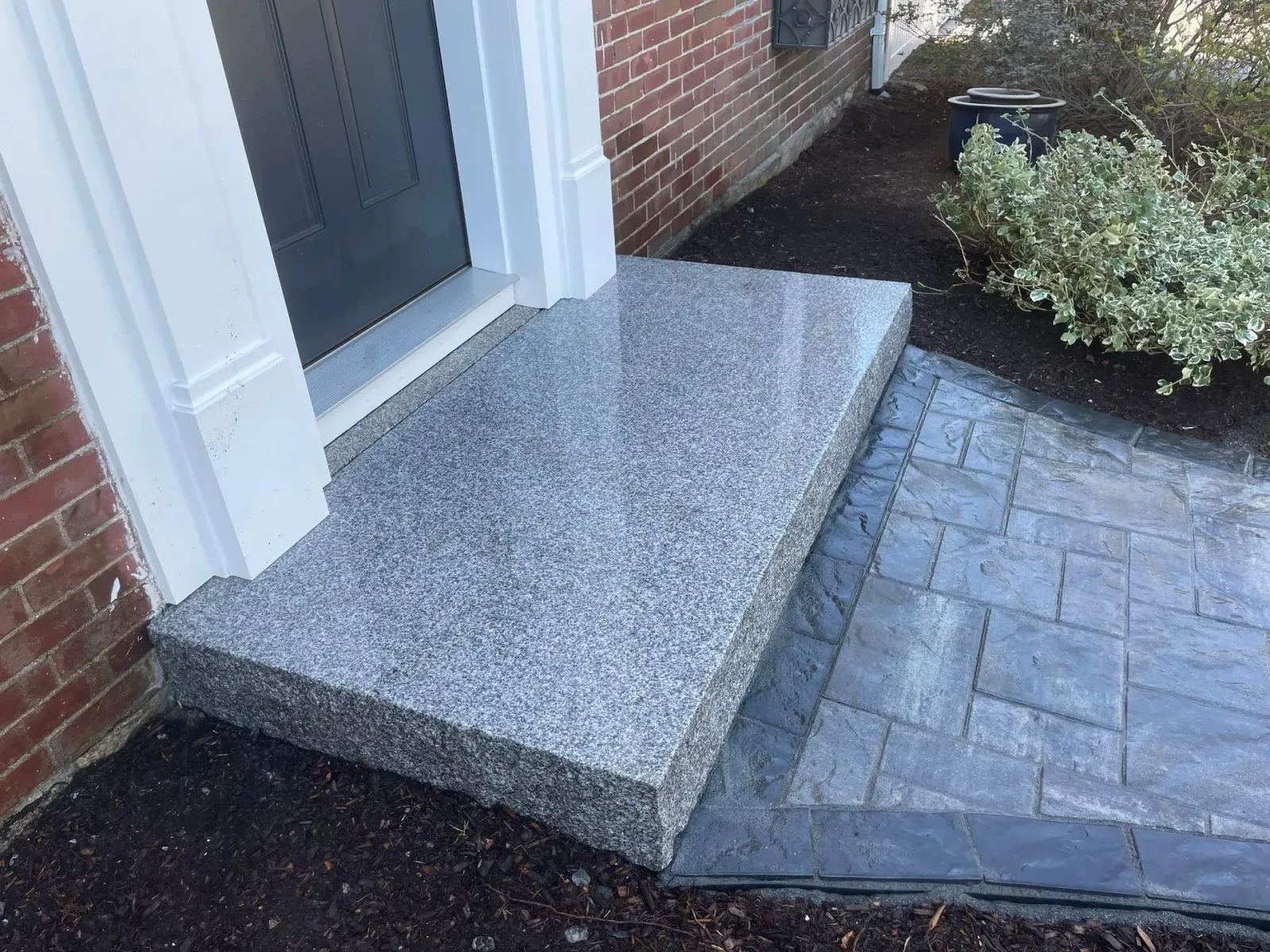 Front entrance with granite step, brick walkway, and small landscaped bed beside a door