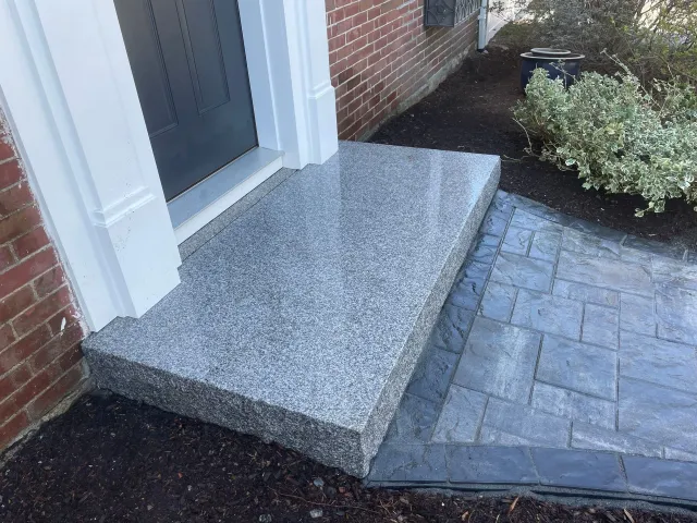 Front entrance with granite step, brick walkway, and small landscaped bed beside a door