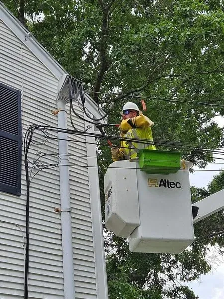 Lineman in bucket truck working on power lines near a house.