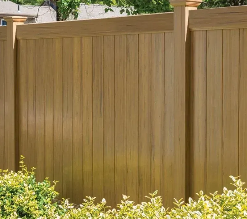 Wooden privacy fence with vertical slats behind green shrubs and a pillar