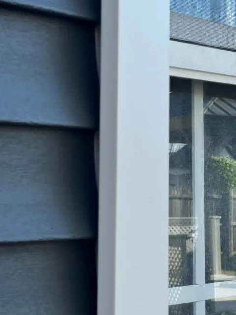 Close-up of dark blue siding beside a white-framed window with a mesh screen