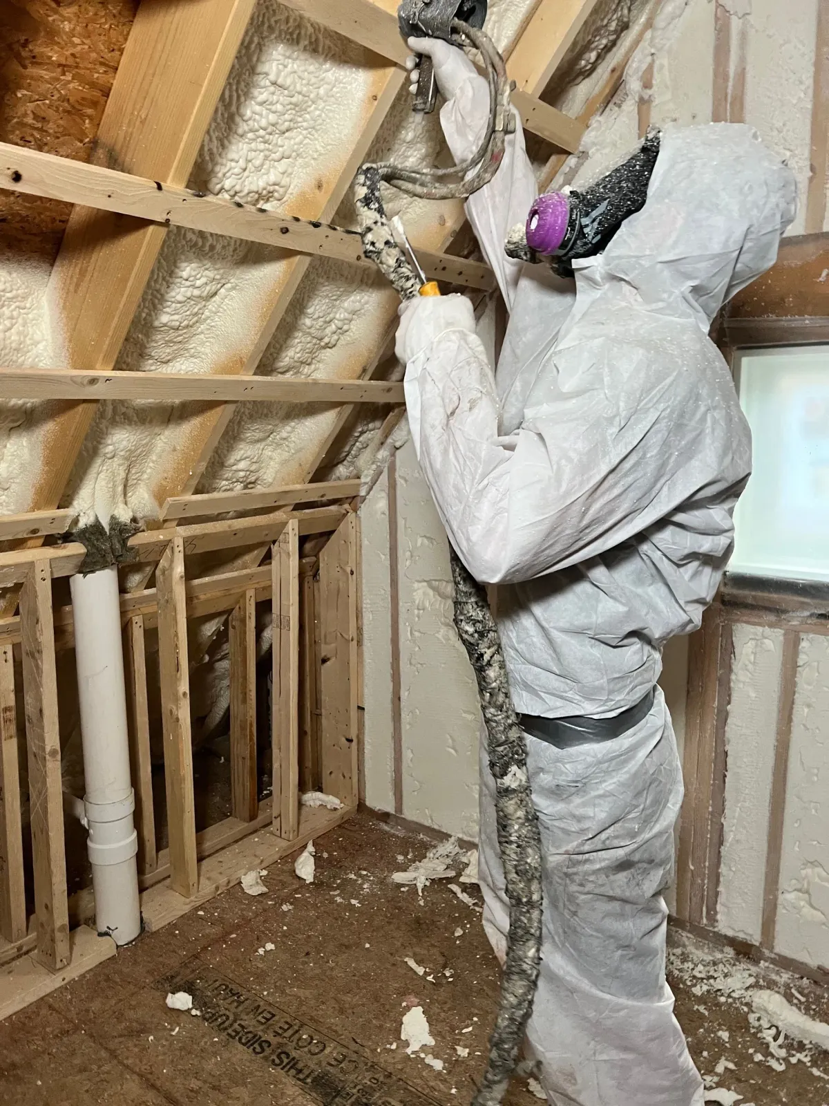 A man is spraying insulation on the ceiling of a room.