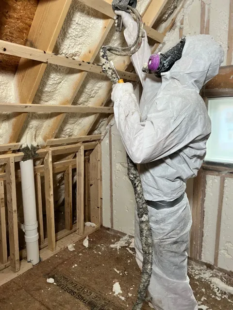 A man is spraying insulation on the ceiling of a room.