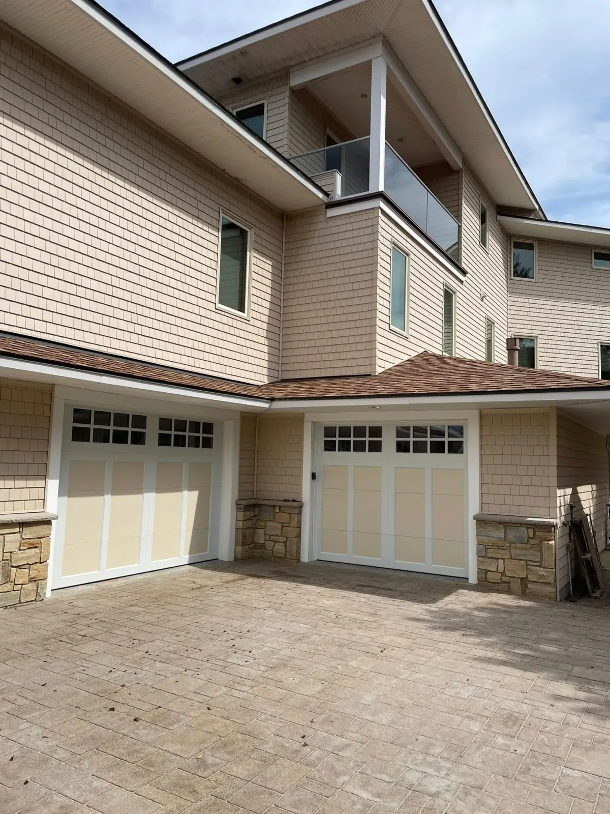 Tan and white house with two garage doors and a gravel driveway.