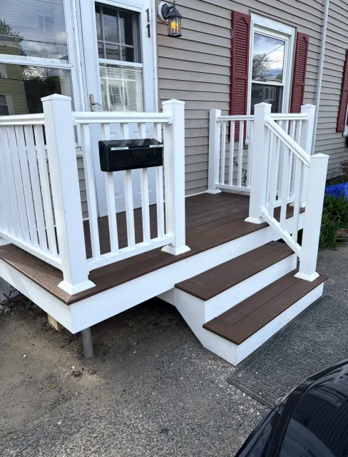 White front porch with brown steps and railing on a house exterior.