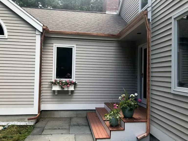 Small townhouse patio with potted flowers, gray siding, and wooden steps leading to a side door.