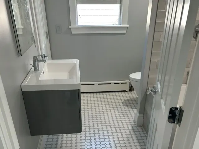 A bathroom with a sink , toilet , mirror and window.