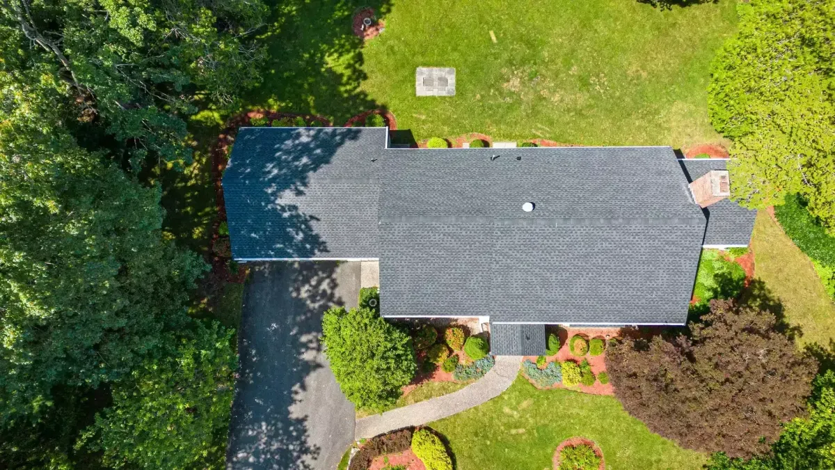 Aerial view of a residential roof with dark shingles, surrounded by landscaped garden and trees, emphasizing Crown Roofing's expertise in roof maintenance and replacement services.