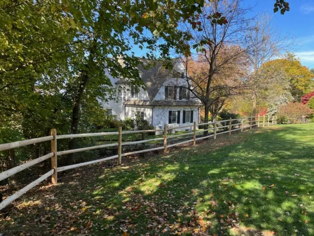 White farmhouse behind a wooden fence along a leafy path in autumn sunlight
