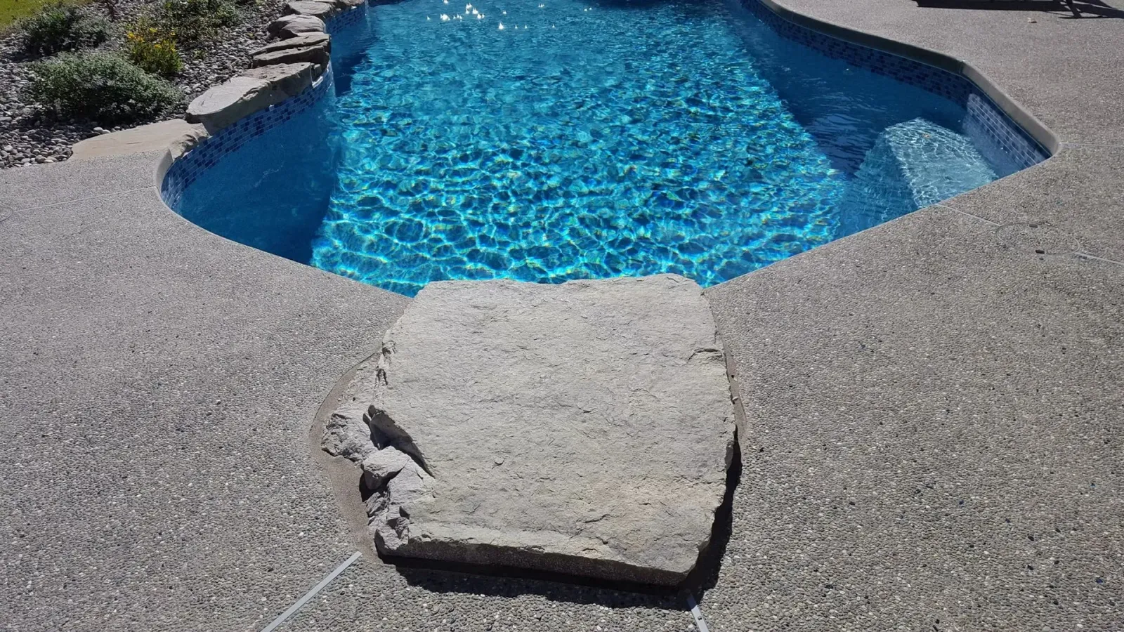 Pool with blue water and stone steps surrounded by a textured concrete deck.