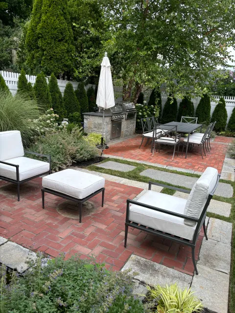 The landscape design of this Newburyport patio garden includes a series of brick and granite patios for a fountain side sitting area and a outdoor kitchen and dining space.