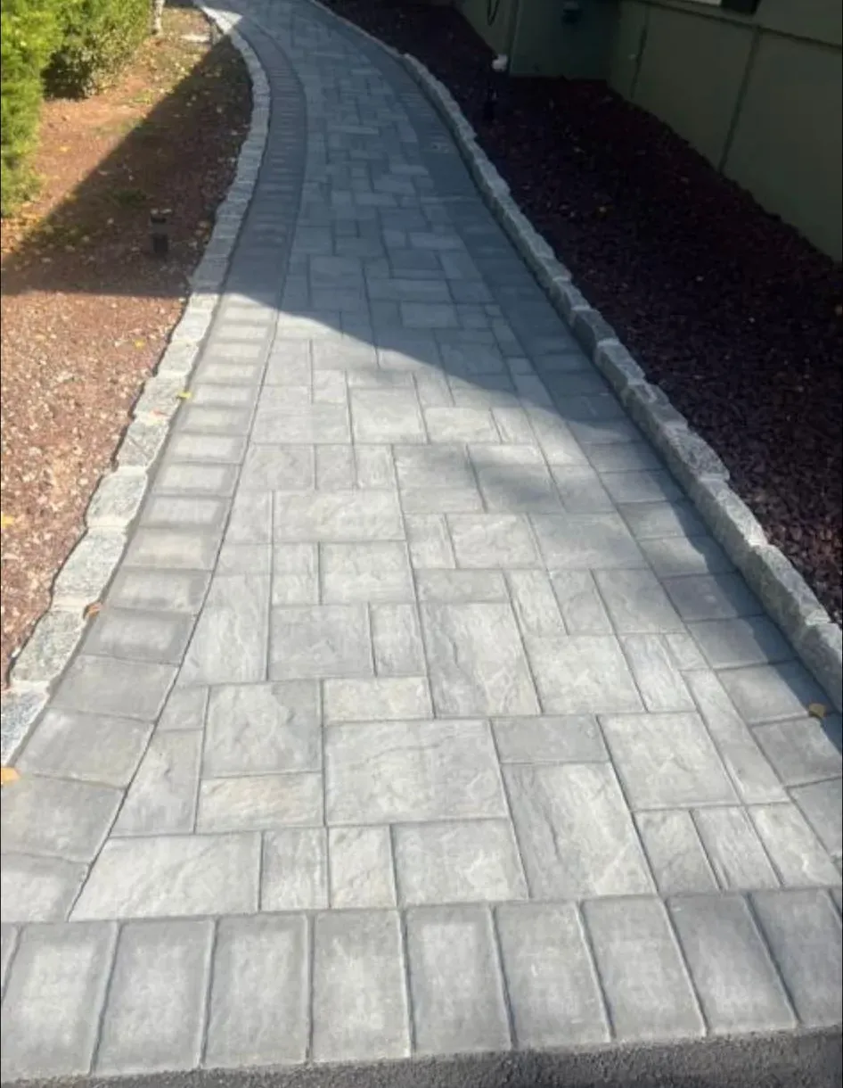 Paved stone walkway curving between landscaped beds beside a building