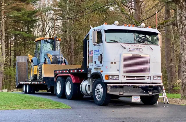 A semi truck is pulling a trailer with a tractor on it.