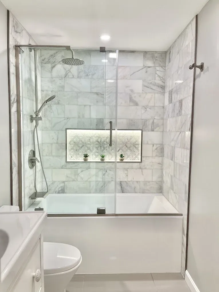 a crisp white and grey remodeled bathroom with recessed lighting installed in the shower and lighting in the shower inset