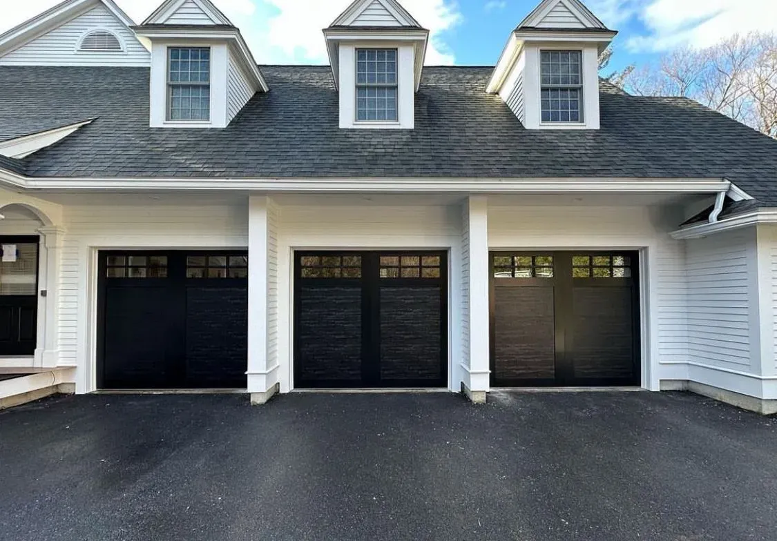 A white house with black garage doors and a gray roof