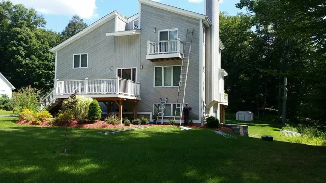 Two-story gray house with balconies and a large green lawn beside trees