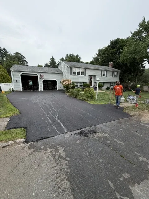 Crew finishing a new asphalt driveway at a split-level home