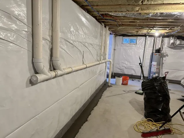Basement with white insulated walls, exposed pipes, and tools on the floor during renovation.