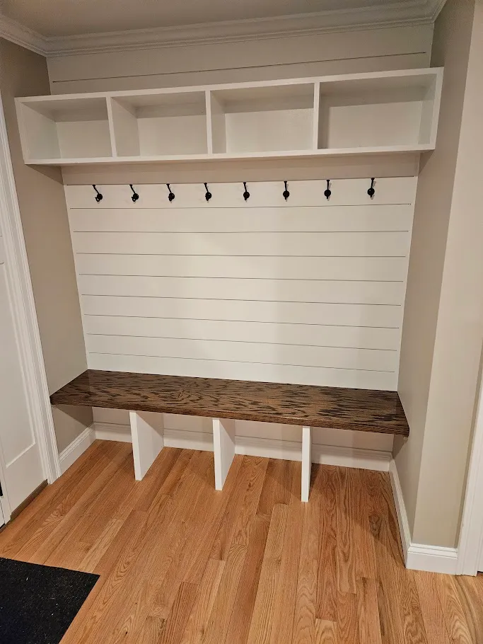 Custom mudroom built-in with white shiplap wall, cubby shelf, black coat hooks, and a stained wood bench by Toensing Construction in Rhode Island