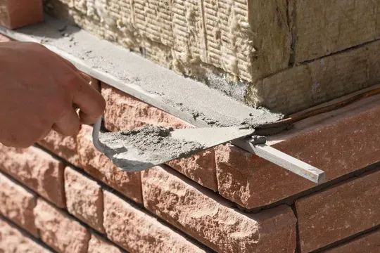 Hand trowel smoothing mortar along a brick wall corner outdoors