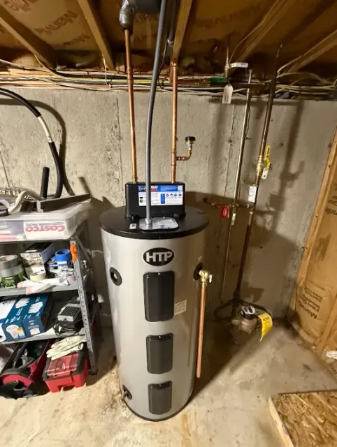 Basement water heater with control panel, exposed pipes, and utility clutter around it