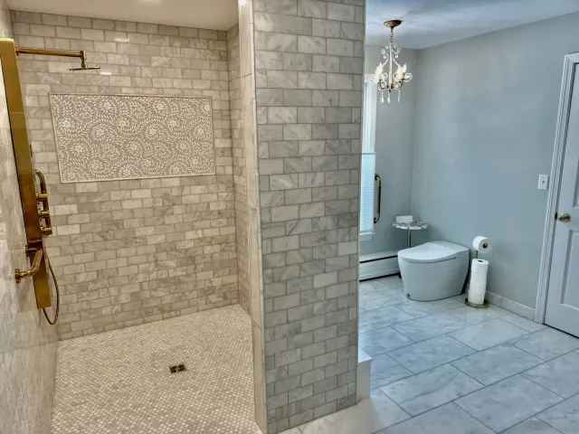 Bathroom with tiled shower on left and separate toilet area on right, in light neutral colors