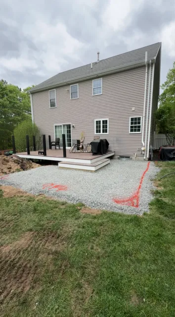 Back of house with deck and gravel patio under construction on a cloudy day.
