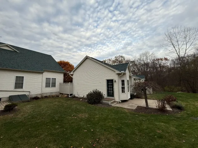 Small white house with green roof and attached garage on a cloudy day