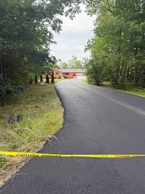 Long freshly paved driveway curving to a red ranch home through the trees