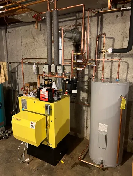 Yellow industrial boiler beside a large gray water heater in a utility room with exposed pipes and ductwork